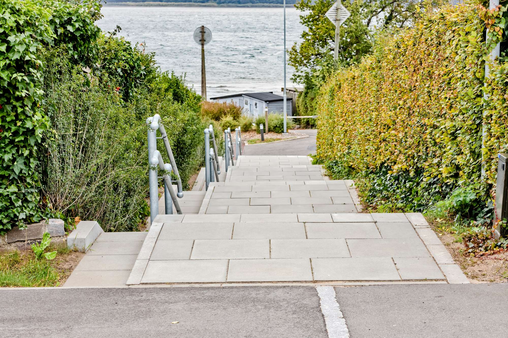 Stentrappe der leder ned mod vandet ved Svendborgsund, omgivet af grønne hække.