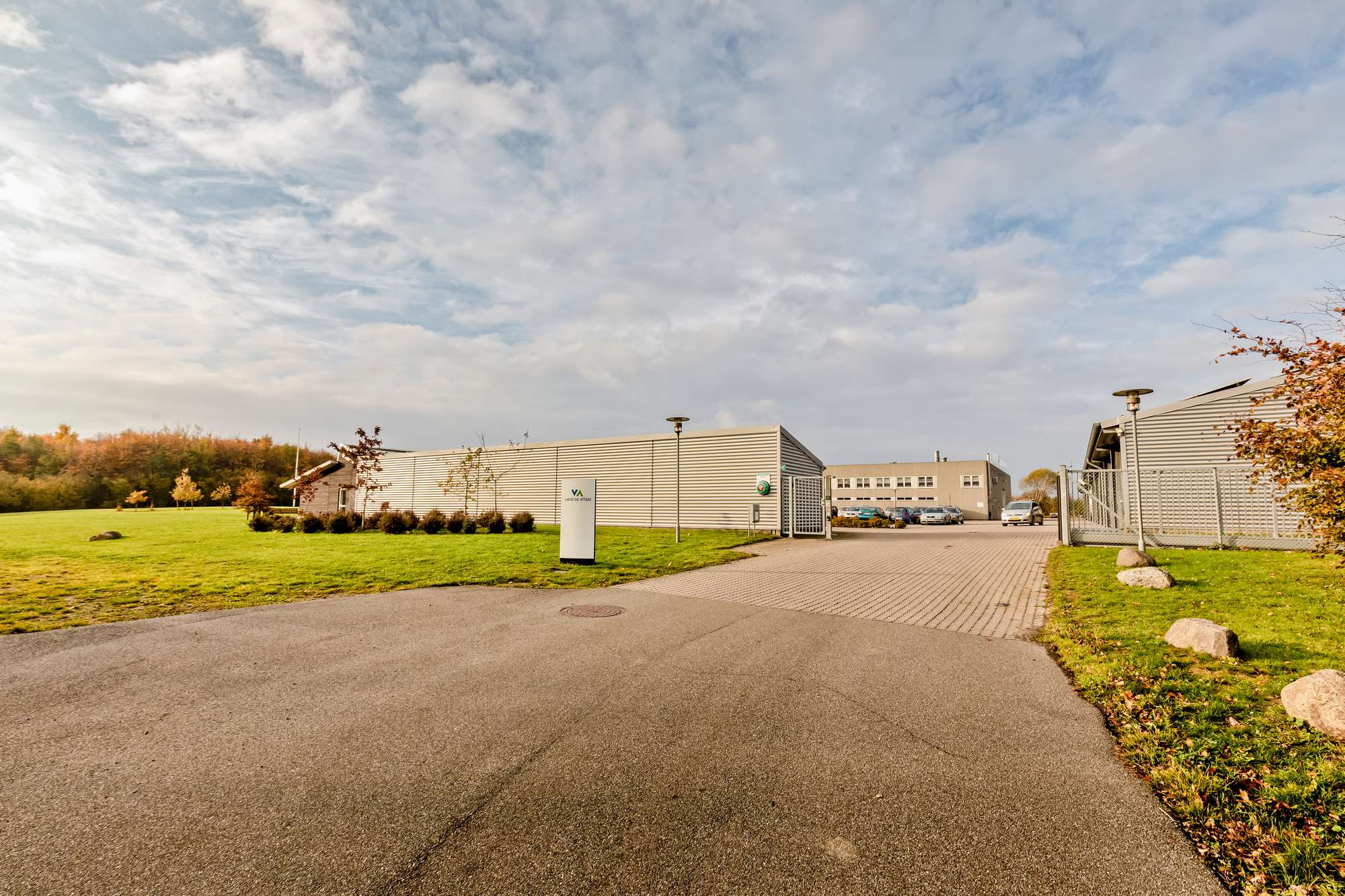 Indkørslen til vores administration på Ryttermarken, grå bygning og grønne omgivelser.